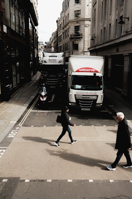A street scene showing a small, clearly marked moving van for a house removal, operated by Movers Barnes, parked in a narrow urban road lined with multi-storey buildings with traditional architecture.